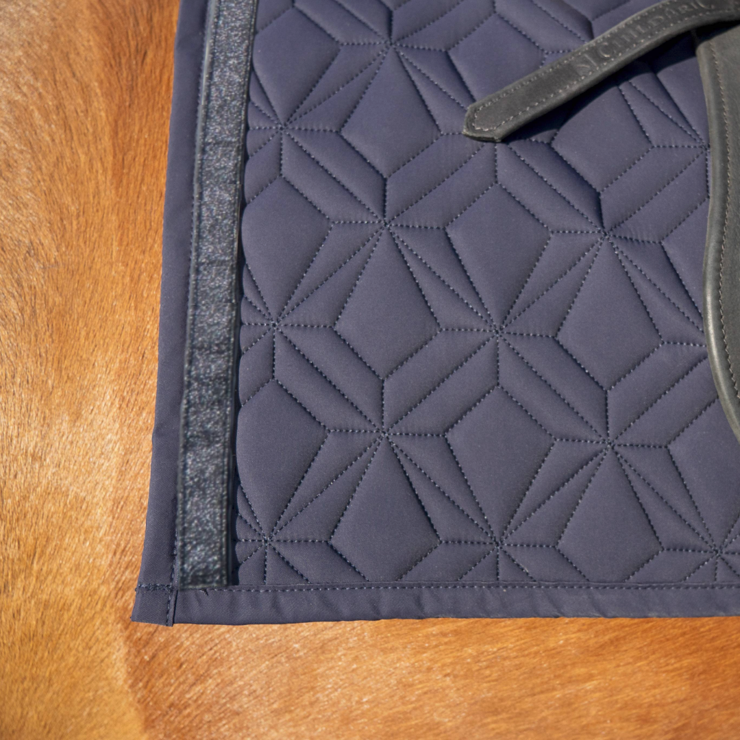 Blaue Schabracke im Detail mit schwarzem Glitzer Klettband. Im Hintergrund sieht man fuchsfabenes Pferdefell.
