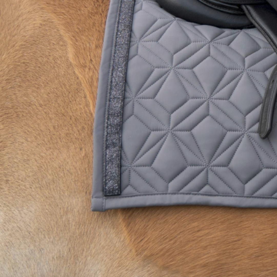 Graue Schabracke im Detail mit schwarzem Glitzer Klettband. Im Hintergrund sieht man fuchsfabenes Pferdefell.