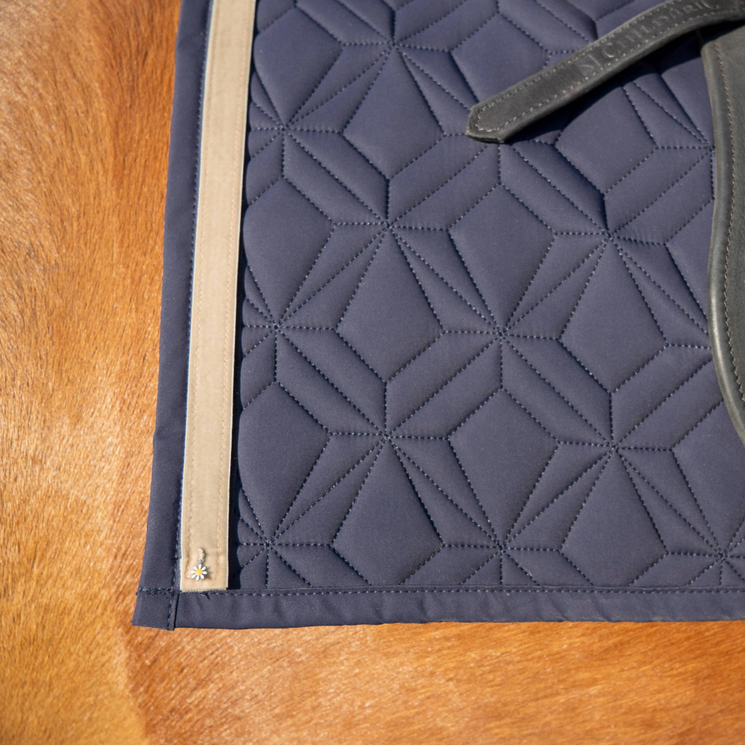 Blaue Schabracke von ROSS KANI mit beigem Frühlingsband und Gänseblümchen-Charm auf dem Pferd.