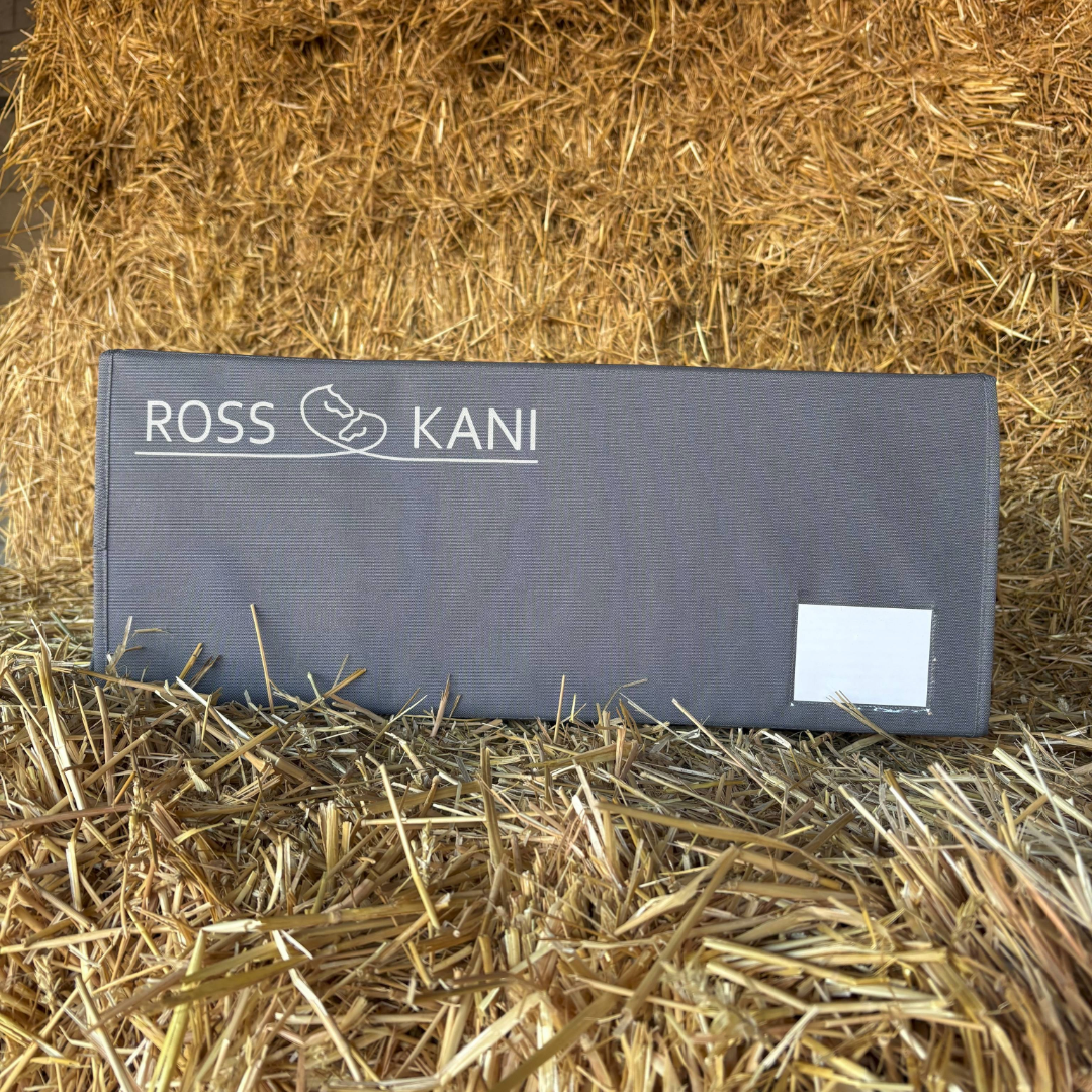 Graue ROSS KANI Aufbewahrungsbox für Schabracken mit Logo, stehend auf Stroh im Stall – praktische Schabrackenbox zur staubfreien Aufbewahrung.