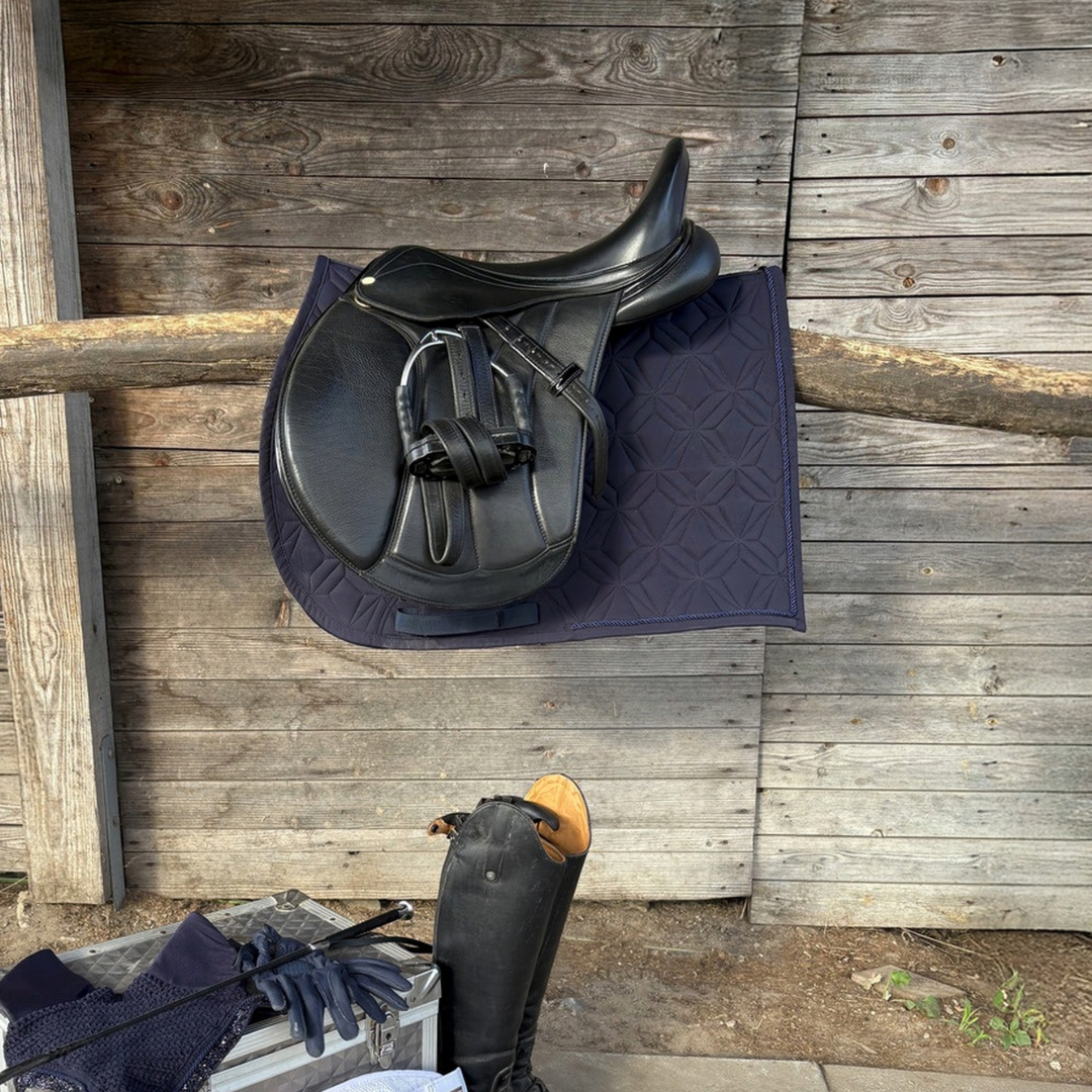 Dunkelblaue ROSS KANI Classic Spring-Schabracke mit schwarzem Springsattel und Reitzubehör vor einer Holzwand