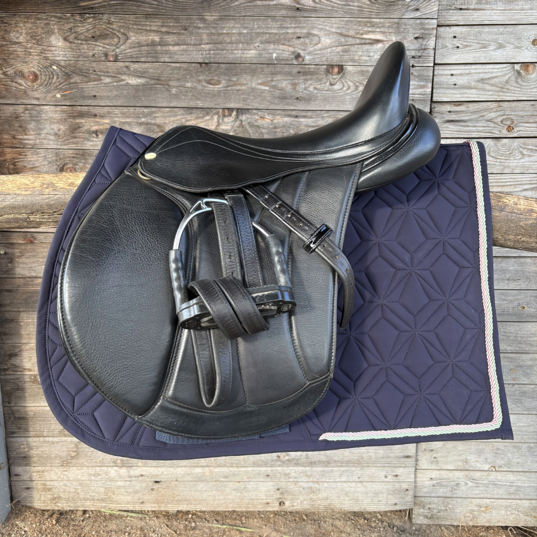 Dunkelblaue ROSS KANI Classic Spring-Schabracke mit zweifarbigen Kordeln und schwarzem Springsattel vor einer Holzwand
