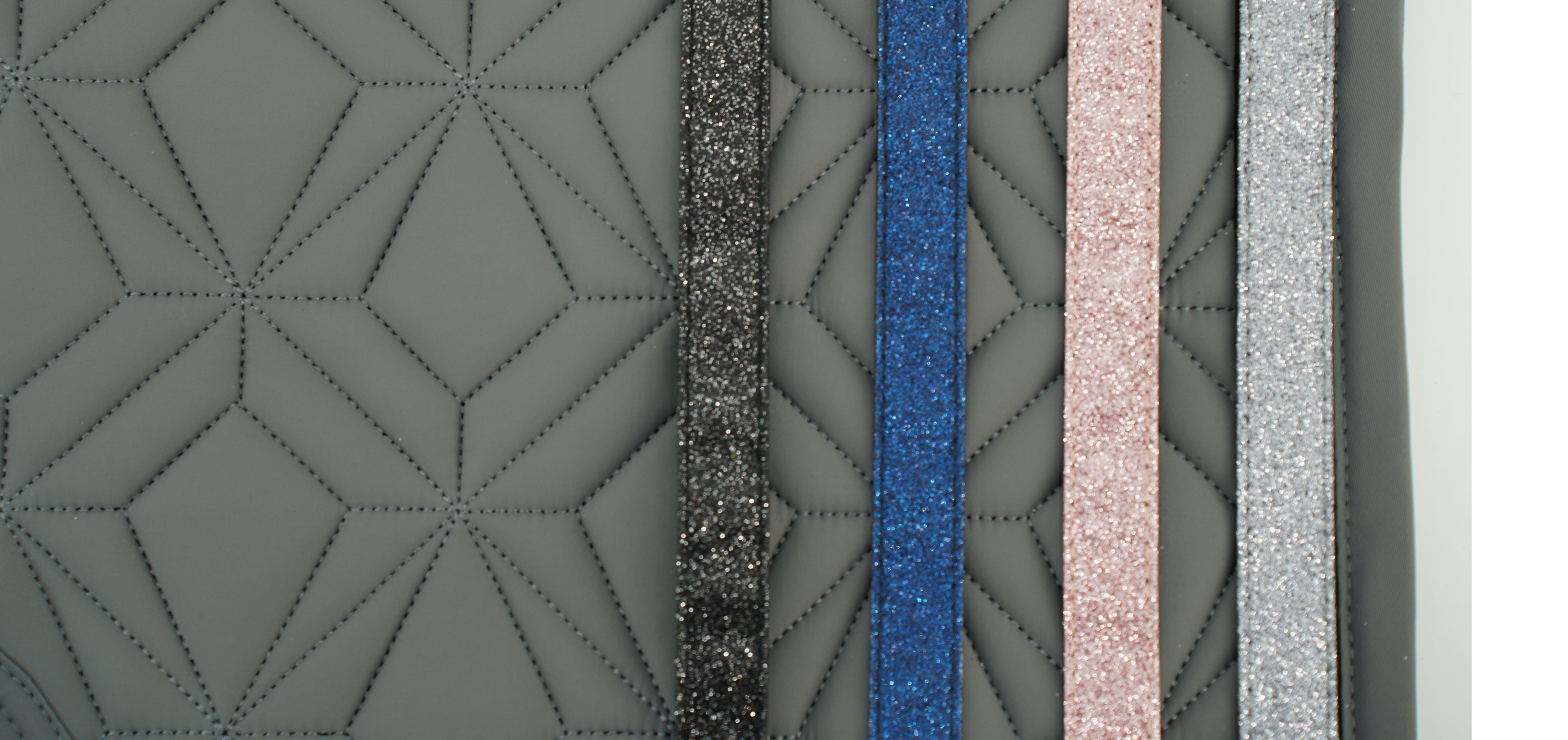 Man sieht die graue Diamant-Steppung der Hautschabracke von ROSS KANI. Auf der Schabracke liegen nebeneinander angeordnet die Glitzerbänder in den Farben schwarz, blau, rosa und grau.