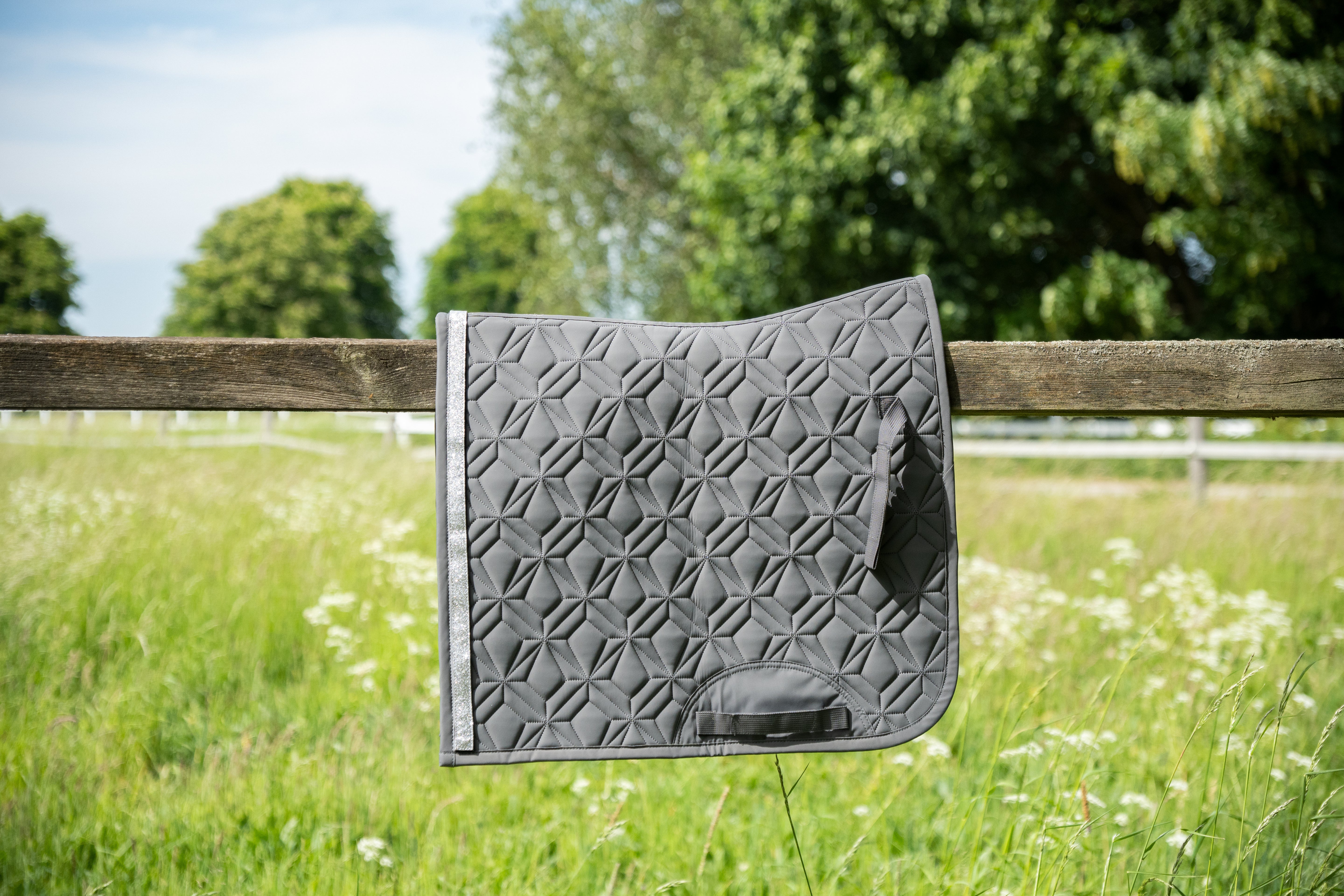 Graue Hauptschabrache von ROSS KANI für die Dressur liegt über Koppelzaun - im Hintergrund Wiese und Büsche - man sieht die elegante Steppung und das edle Design der Schabracke