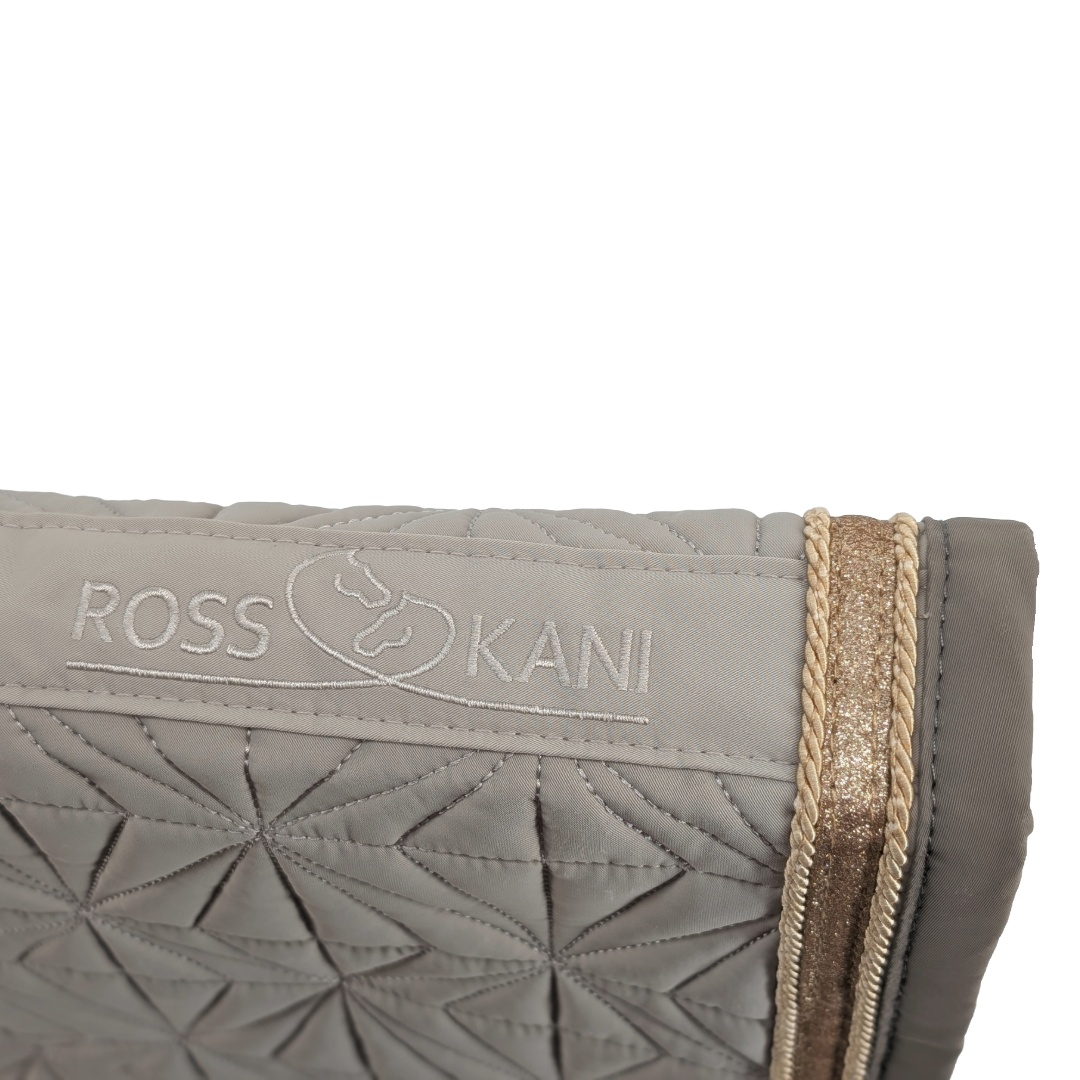 Detailaufnahme des gesteppten ROSS KANI Logos auf dem beigen Schabracken-Cover – goldene Kordel, goldenes Glitzerband.