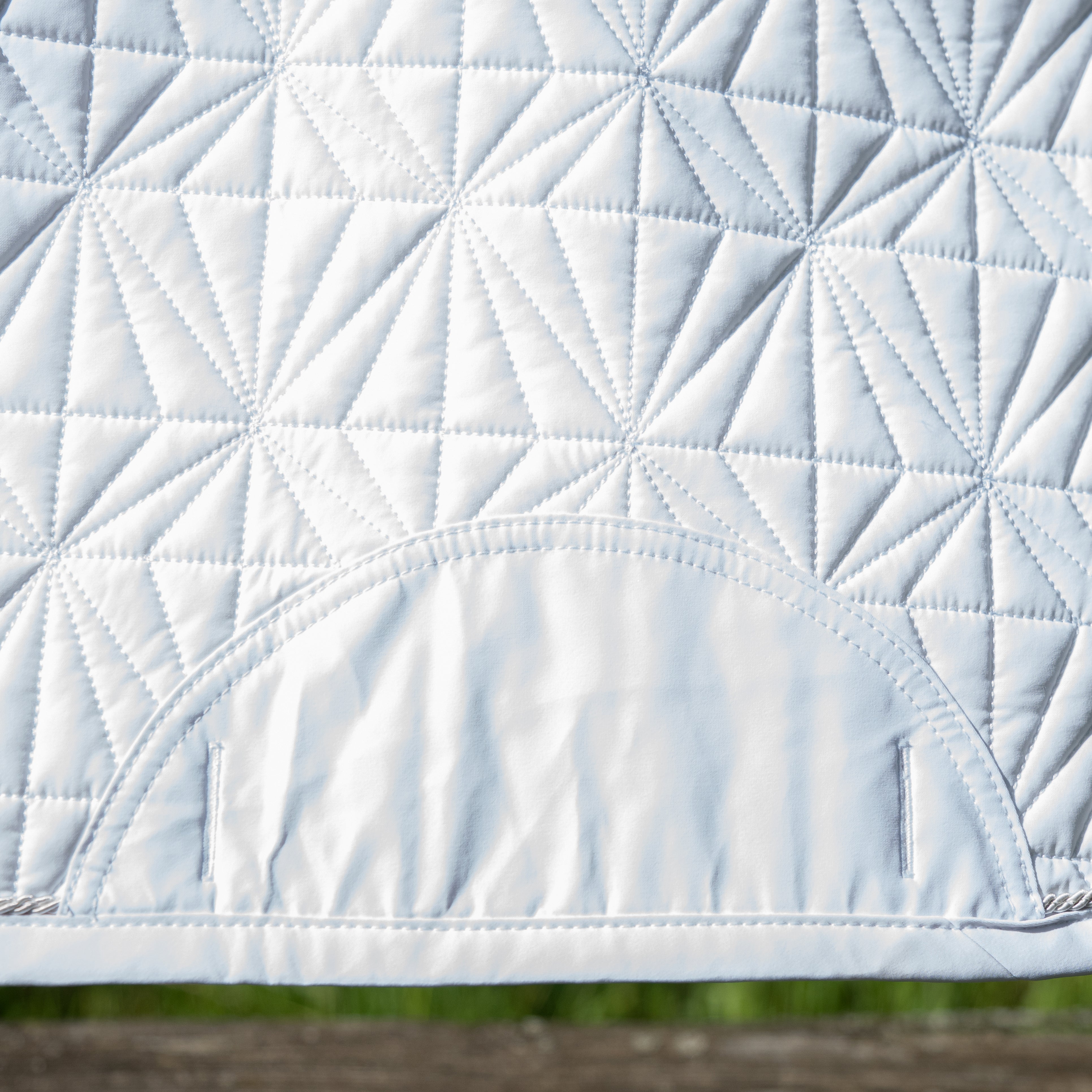 Detailansicht des weißen ROSS KANI Schabracken-Covers mit geometrischem Steppmuster und robusten Gurtschlitzen – elegantes und funktionales Reitzubehör.