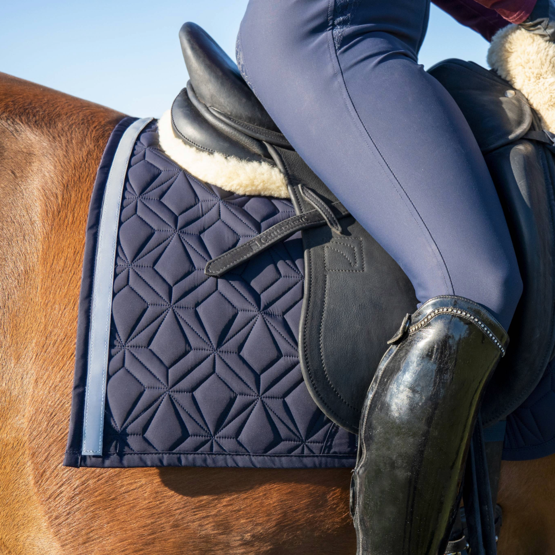 Blaue Dressur-Schabracke von ROSS KANI mit reflektierendem Klettband in Silber. Die Schabracke liegt auf einem fuchsfarbenem Pferd, darauf liegt ein schwarzer Sattel.