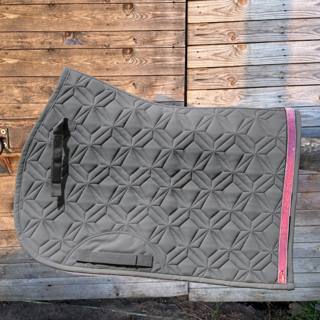 Graue Springschabracke von ROSS KANI mit rosa Frühlingsband und Eis-Charm vor einer Holzwand.