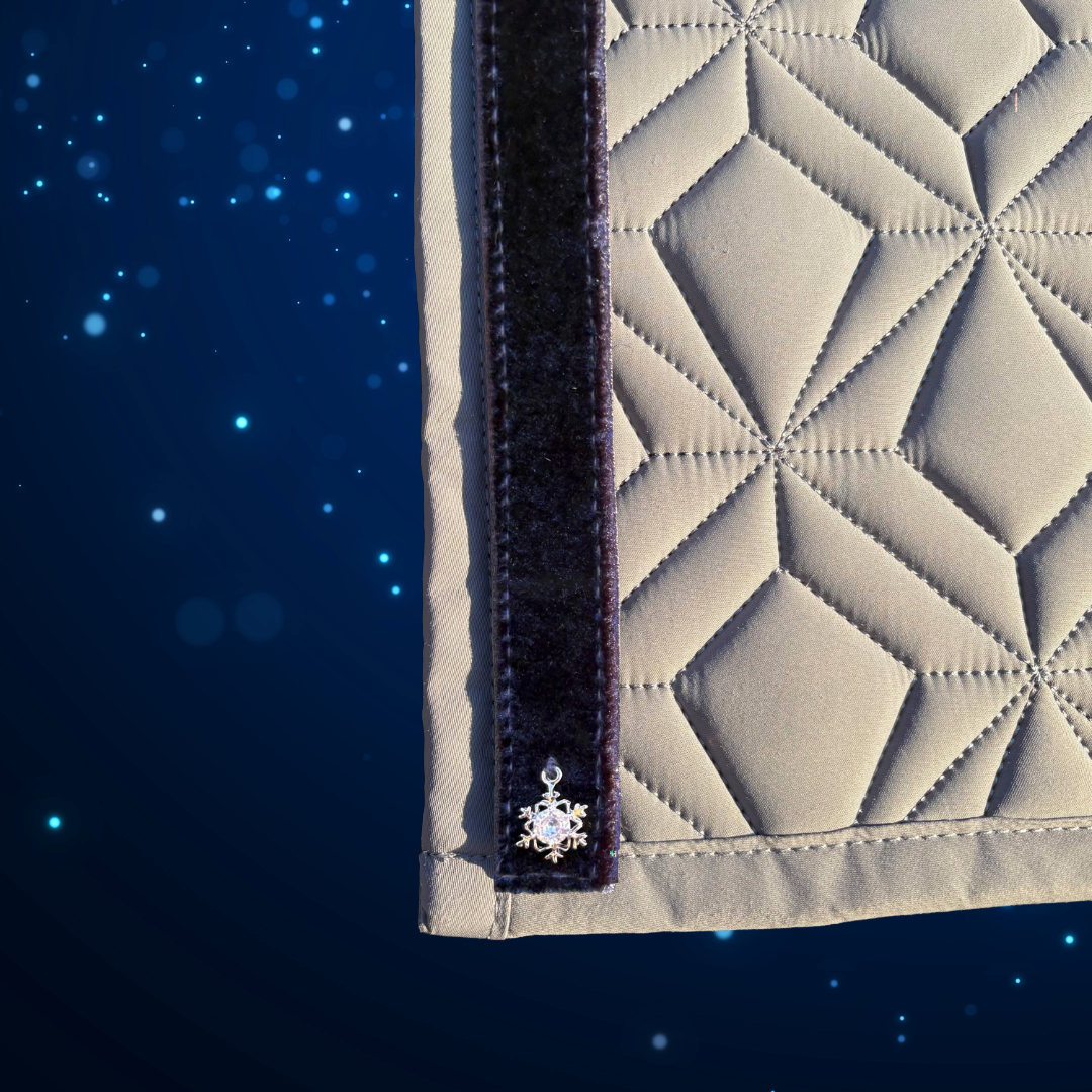 Detailansicht der grauen Schabracke von ROSS KANI mit seitlichem dunkelblauem Samtstreifen, verziert mit einem kleinen silbernen Schneeflocken-Anhänger vor blauem Hintergrund