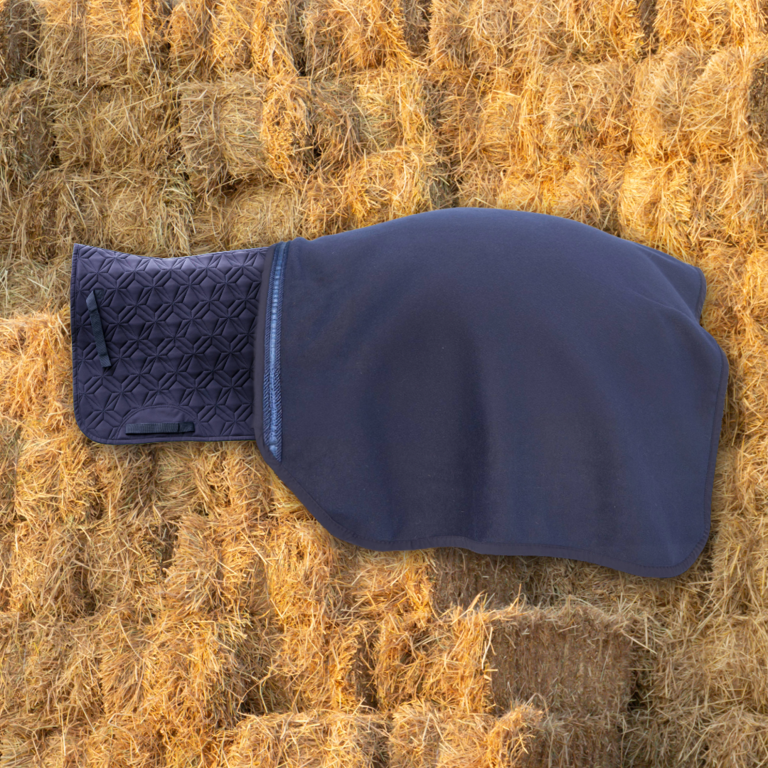 Die Wollwalk-Ausreitdecke ist mit Klett an der dunkelblauen Hauptschabracke von ROSS KANI befestigt ; im Hintergrund sind Strohballen.