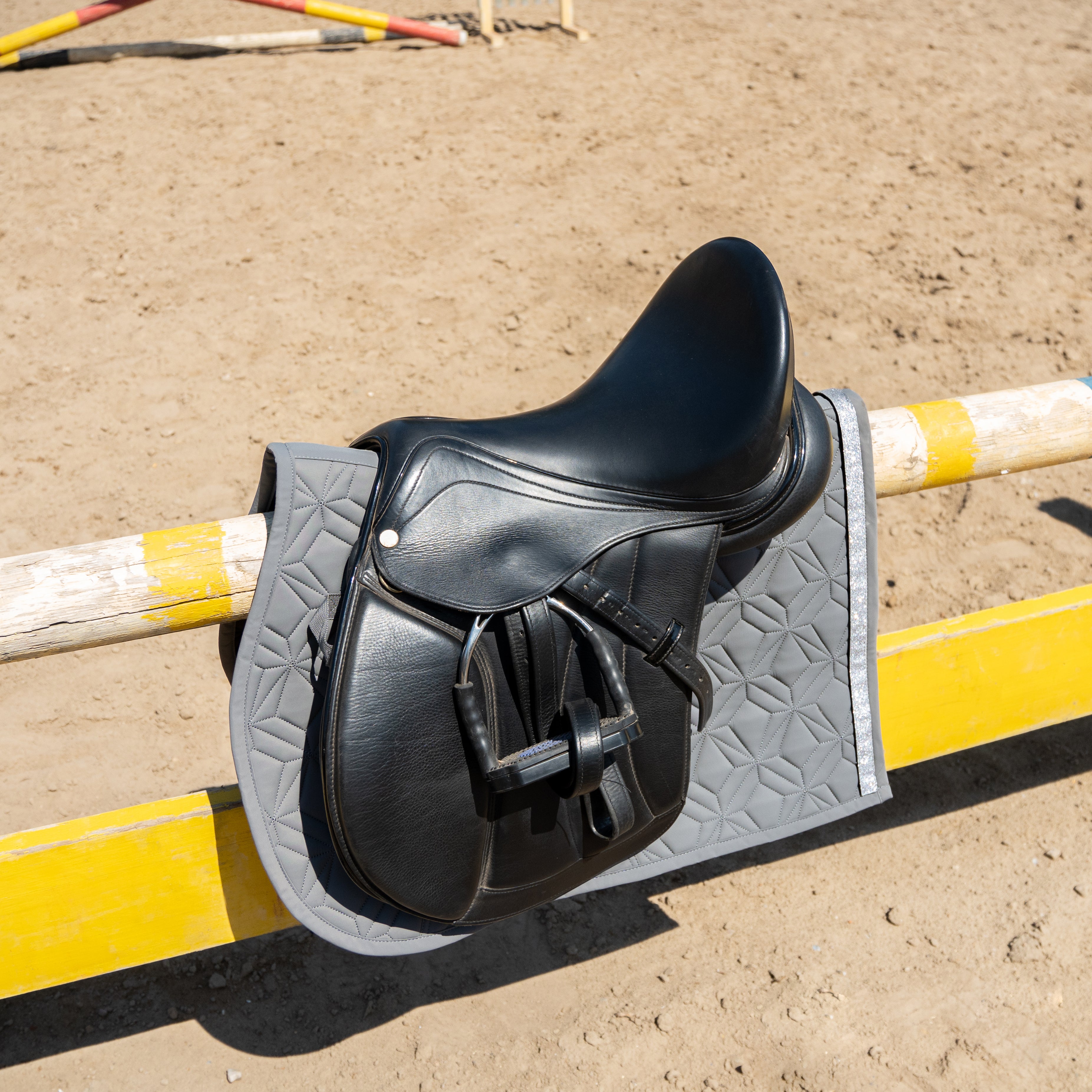 Graue Spring-Schabracke von ROSS KANI unter Sattel auf Springstange in Seitenansicht – elegante Steppung und anatomische Passform.