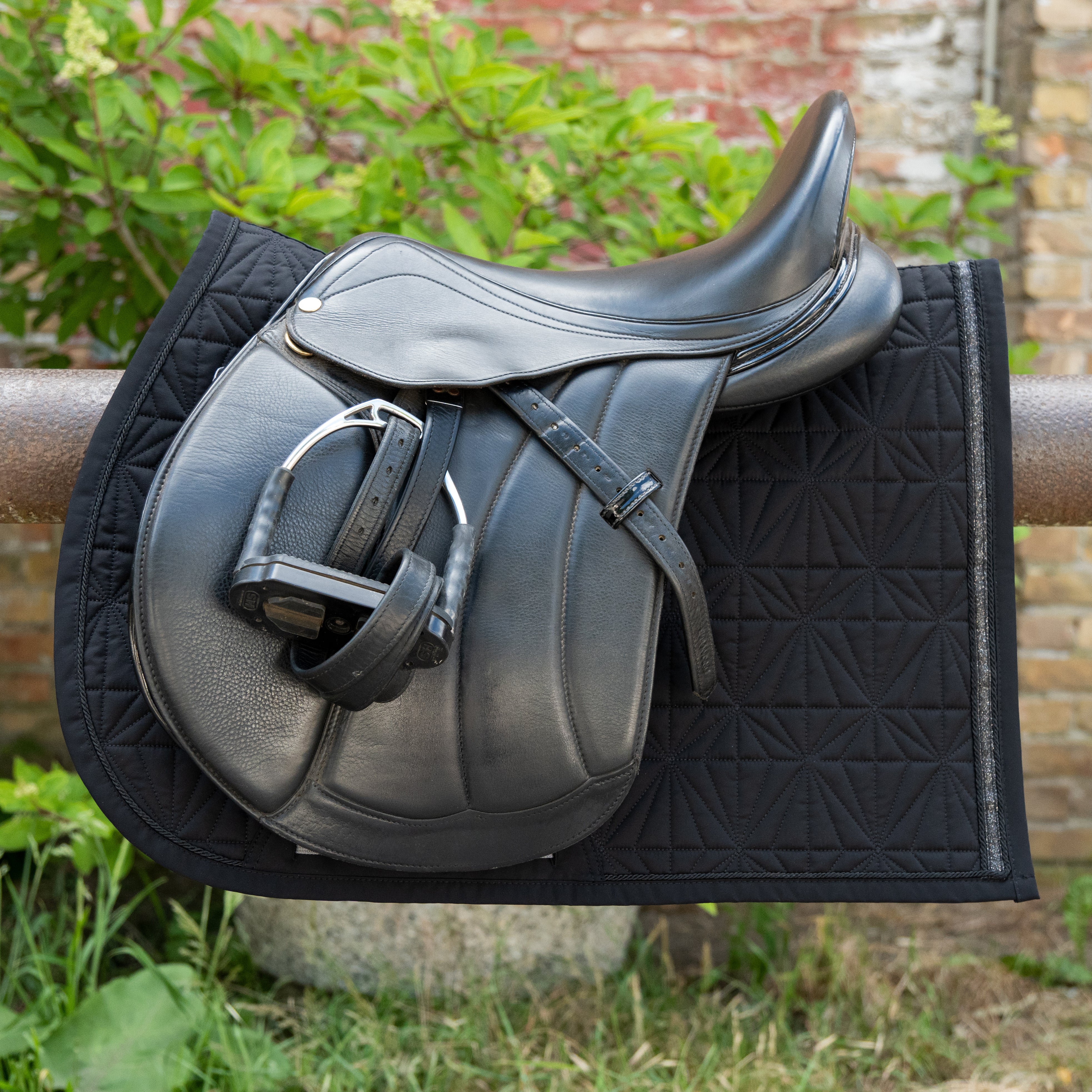 Detailbild eines schwarzen ROSS KANI Schabracken-Covers mit geometrischem Steppmuster unter hochwertigem Vielseitigkeitssattel – elegante, stoßdämpfende Sattelunterlage für anspruchsvolle Reiter.