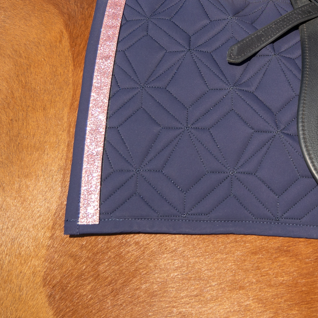 Blaue Schabracke im Detail mit rosa Glitzer Klettband. Im Hintergrund sieht man fuchsfabenes Pferdefell.