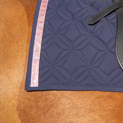 Blaue Schabracke im Detail mit rosa Glitzer Klettband. Im Hintergrund sieht man fuchsfabenes Pferdefell.