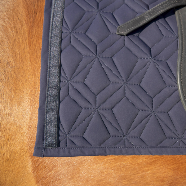 Blaue Schabracke im Detail mit schwarzem Glitzer Klettband. Im Hintergrund sieht man fuchsfabenes Pferdefell.