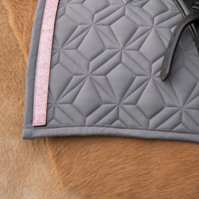 Graue Schabracke im Detail mit rosa Glitzer Klettband. Im Hintergrund sieht man fuchsfabenes Pferdefell.