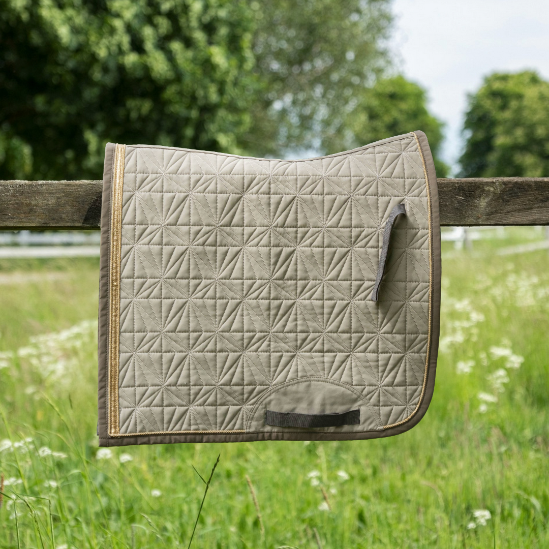 Beiges ROSS KANI Dressur-Cover in Seitenansicht über einem Koppelzaun mit Wiese und Bäumen im Hintergrund– elegante Steppung und anatomische Passform.