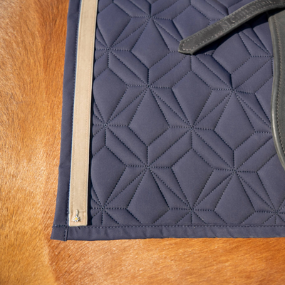 Blaue Schabracke von ROSS KANI mit beigem Frühlingsband und Gänseblümchen-Charm auf dem Pferd.