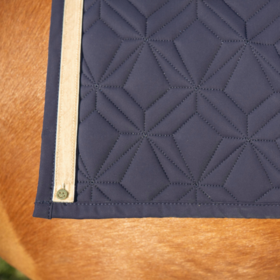 Blaue Schabracke von ROSS KANI mit beigem Frühlingsband und Smiley-Charm unter dem Sattel auf dem Pferd – stilvoller Look beim Reiten. 