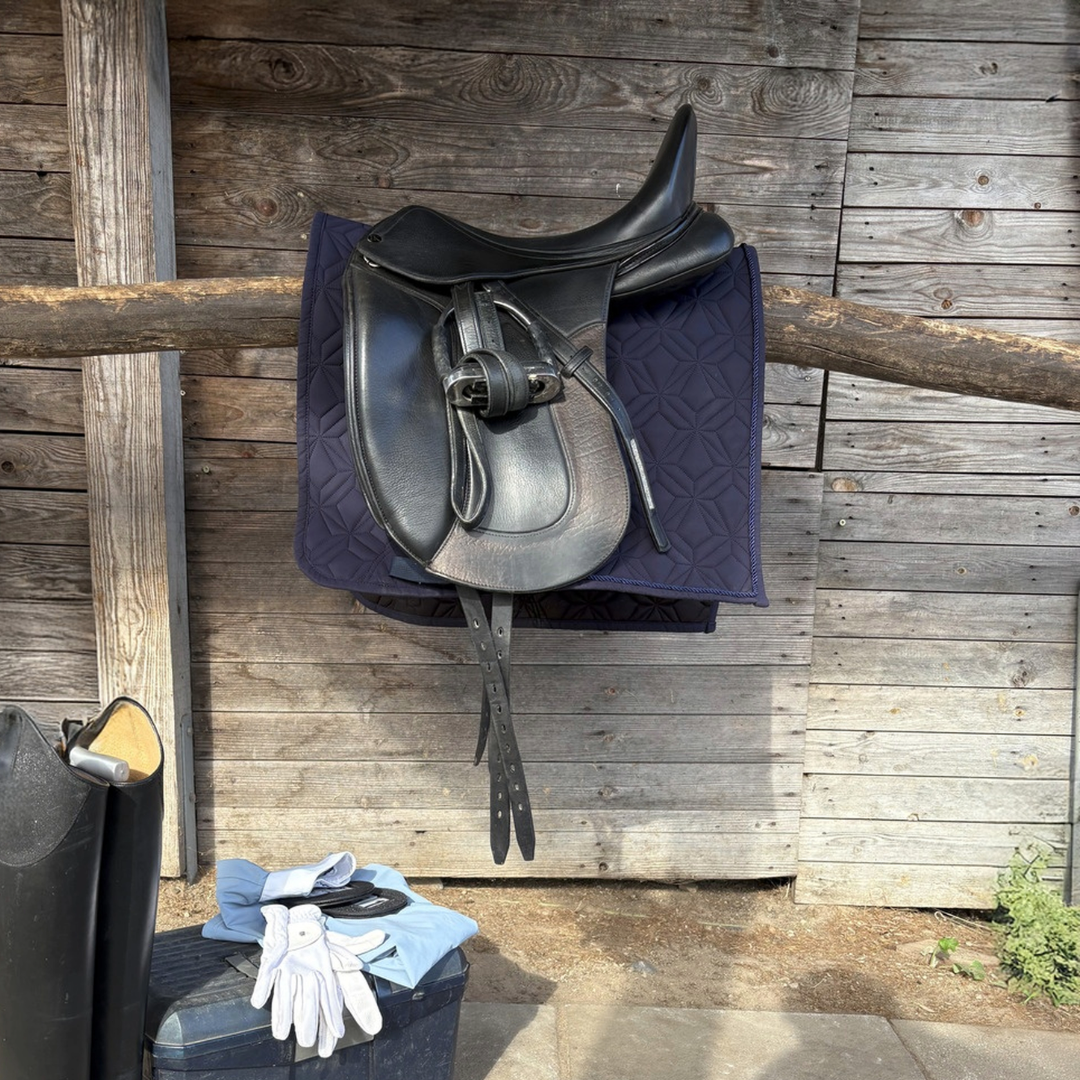 Dunkelblaue ROSS KANI Classic Dressur-Schabracke mit schwarzem Dressursattel vor einer Holzwand im Reitstall