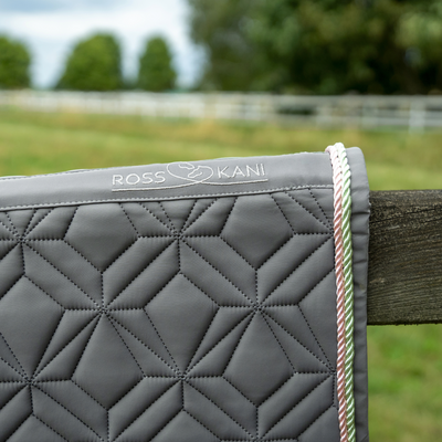 Detailansicht der grauen ROSS KANI Classic Schabracke mit Logo, geometrischer Steppung und rosa-grüner Kordel
