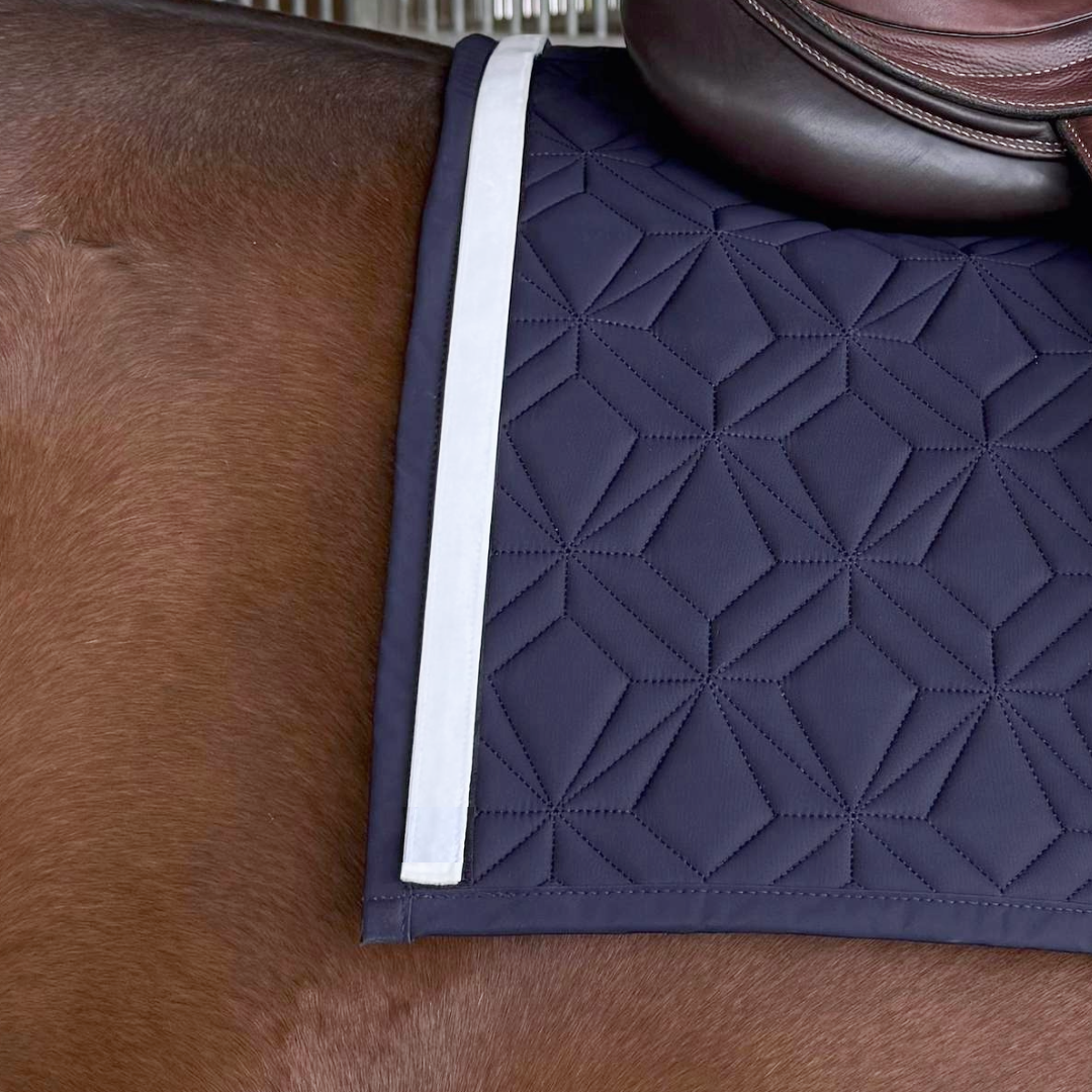 Detailaufnahme einer blauen ROSS KANI Schabracke mit weißem Samtband unter braunem Reitsattel auf einem braunen Pferd