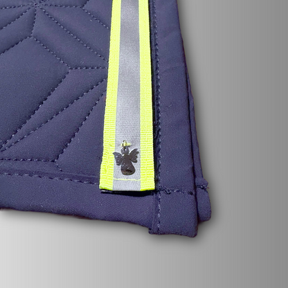 Detailansicht des reflektierenden Neonklettbandes mit Schutzengel-Charm von ROSS KANI auf der blauen Schabracke mit geometrischem Steppmuster.