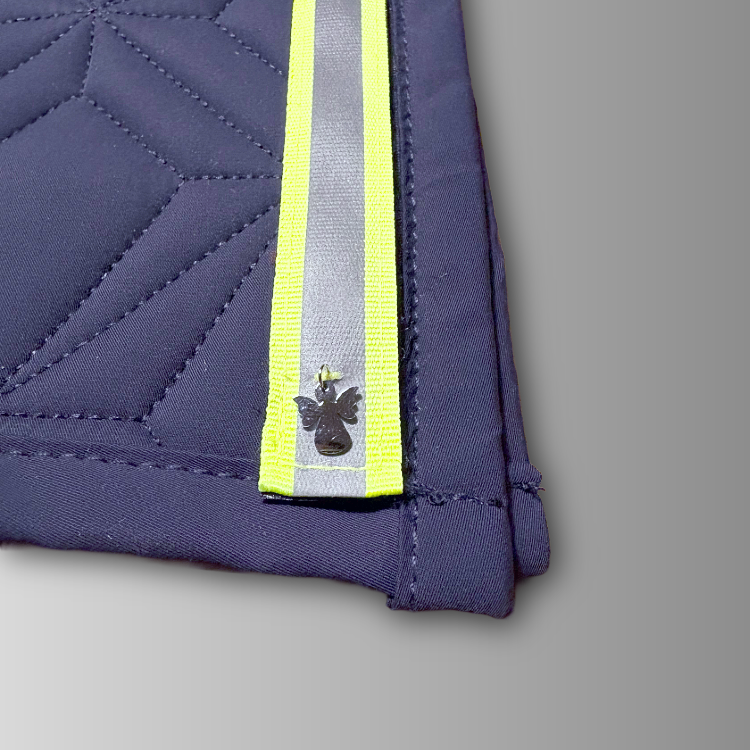 Detailansicht des reflektierenden Neonklettbandes mit Schutzengel-Charm von ROSS KANI auf der blauen Schabracke mit geometrischem Steppmuster.