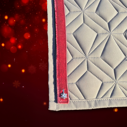 Detailansicht der grauen Schabracke von ROSS KANI mit seitlichem dunkelrotem Samtstreifen, verziert mit einem kleinen silbernen Schneeflocken-Anhänger vor rotem Hintergrund