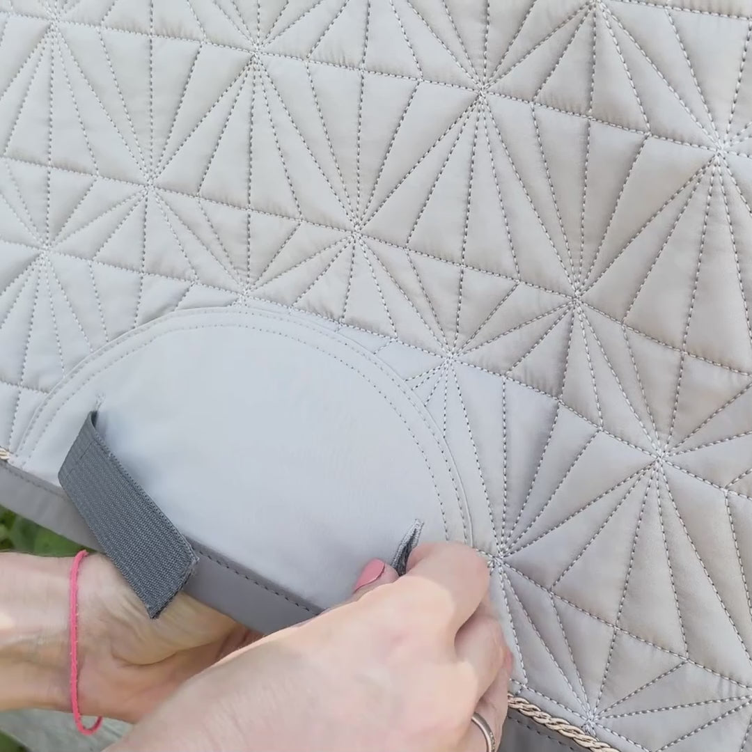 Video laden: Das beige Dressur-Cover wird auf die graue Hauptschabracke von ROSS KANI aufgeklettet. Die Schabracke hängt über einem Koppelzaun und im Hintergrund sieht man Wiese.
