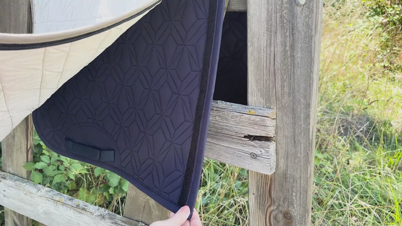 Video: Das beige Dressur-Cover wird auf die blaue Hauptschabracke von ROSS KANI aufgeklettet. Die Schabracke hängt über einem Koppelzaun und im Hintergrund sieht man Wiese.