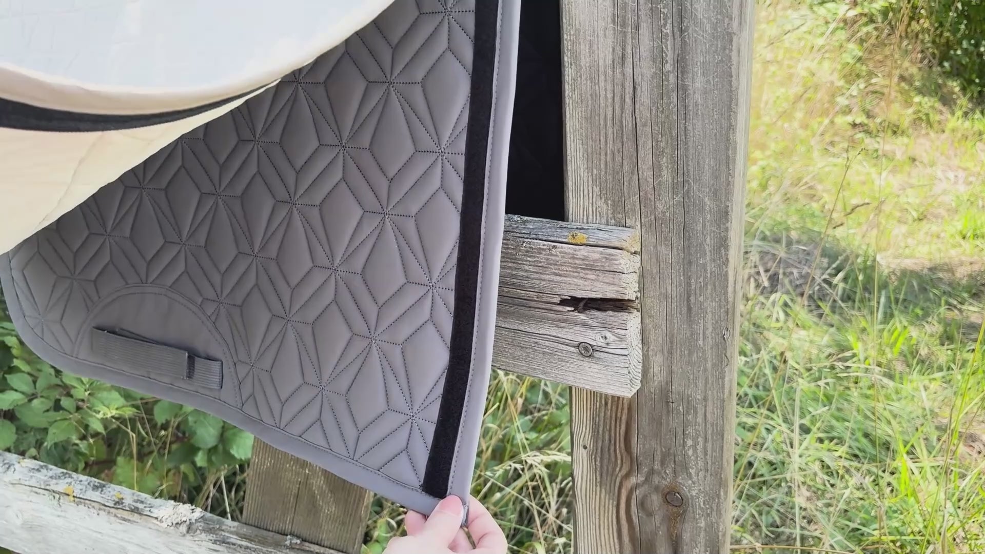 Video laden: Video: Das beige Dressur-Cover wird auf die graue Hauptschabracke von ROSS KANI aufgeklettet. Die Schabracke hängt über einem Koppelzaun und im Hintergrund sieht man Wiese.