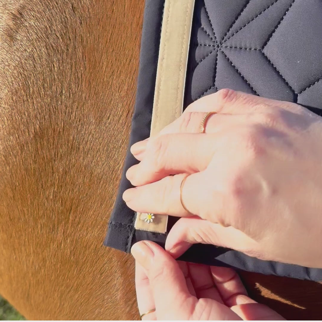 Video laden: Video: Beiges Frühlingsband von ROSS KANI mit Gänseblümchen-Charm ist auf der blauen Schabracke befestigt – einfache Handhabung.